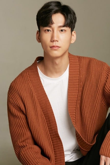 Lee Jun Kyung sitting on a floor wearing light brown outer, white t-shirt and black pant with black hair.